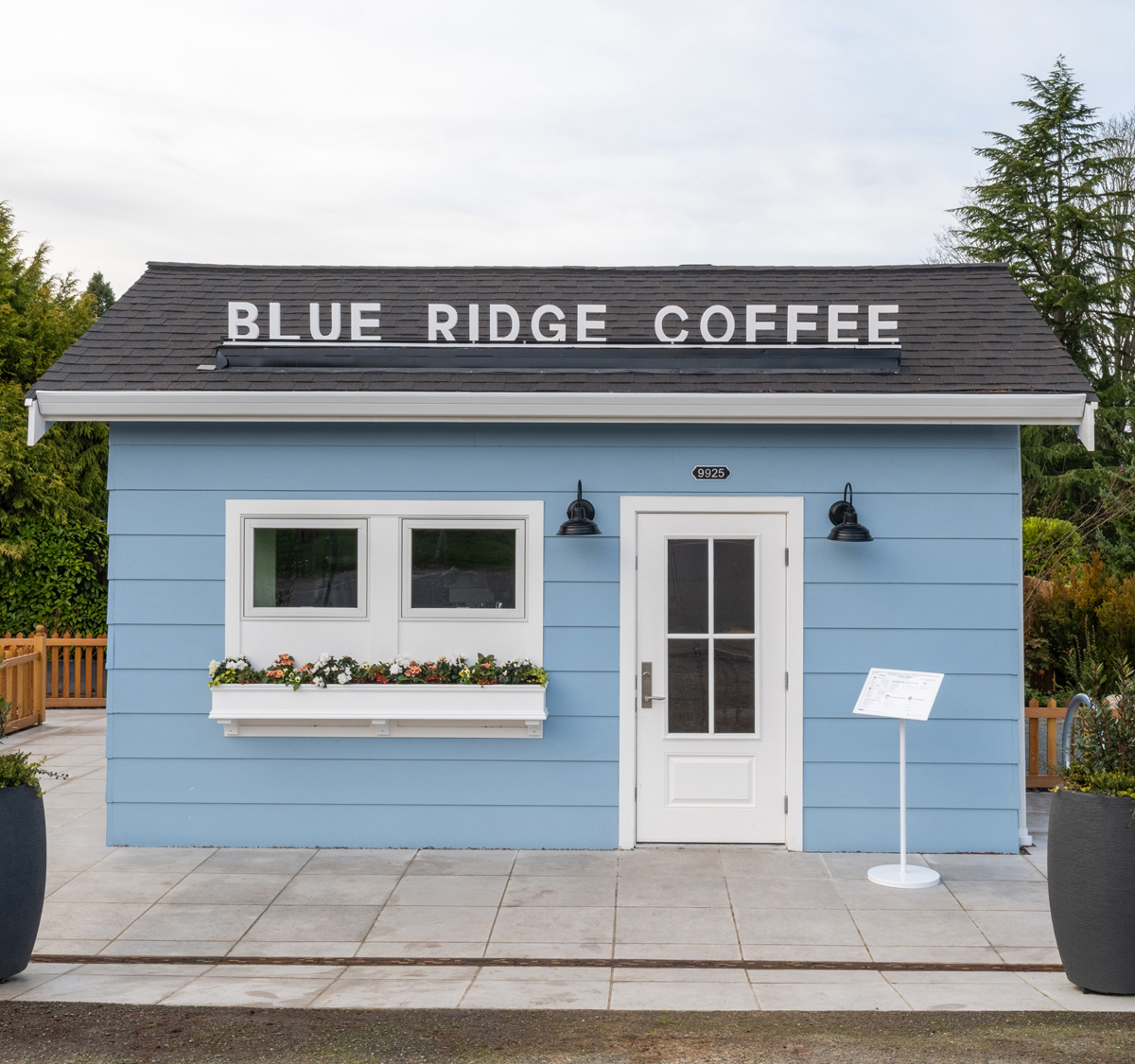 Small light-blue Blue Ridge Coffee building in Seattle with a flower box, white door, and fenced paver patio