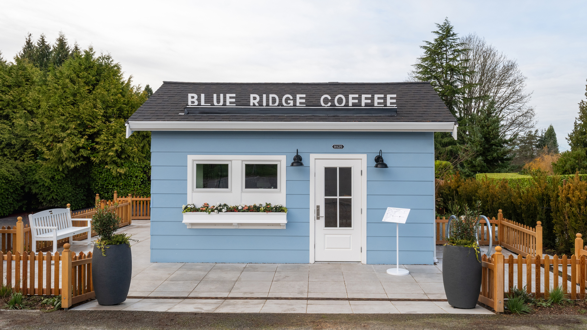 Small light-blue Blue Ridge Coffee building in Seattle with a flower box, white door, and fenced paver patio